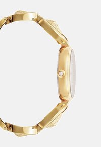 Kultainen rannekello, jossa on pyöreä kotelo, teksturoitu linkkiranneke ja keskikruunu. Kellotaulu on hopeanvärinen, hienovaraisilla merkinnöillä eikä numerotietoa.