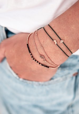 Set aus gestapelten Armbändern mit roségoldenen Ketten, schwarzen und goldenen Perlen sowie grünen Schnüren, einschließlich Anhängern in Form eines Blattes und eines Fisches.