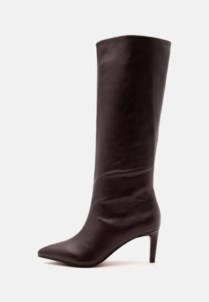 Botte haute en cuir marron foncé avec bout pointu et talon fin de hauteur moyenne, vue de profil sur fond blanc.