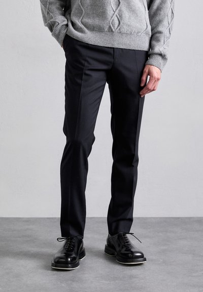 Pantaloni negri, cu croi elegant și textură netedă, asortați cu pantofi negri lucioși și un pulover texturat de culoare gri deschis.