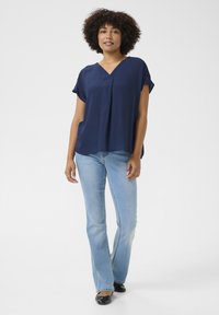 Blouse bleu marine à manches courtes avec un col en V, en tissu texturé, associée à un jean flare bleu clair et des ballerines noires. Style simple et décontracté.