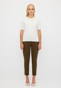 Vit kortärmad topp med blomsterlacemönster vid kragen, kombinerad med slim-fit olivgröna byxor och ljusrosa klackar.