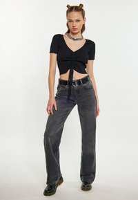 Černý žebrovaný crop top s krátkými rukávy a detailem na stažení, zkombinovaný s volnými, bledými černými širokými džíny a černými botami Dr. Martens.