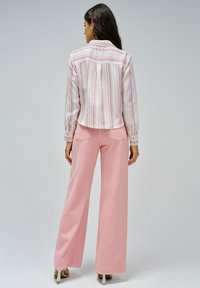 Camisa corta a rayas en tela blanca y rosa con puños de botón, combinada con pantalones rosas de pierna ancha que cuentan con bolsillos traseros y una textura suave.
