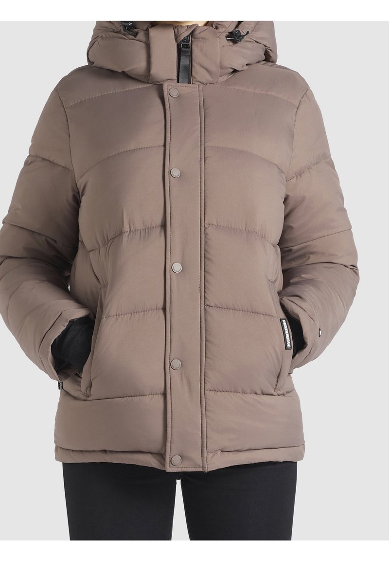Chaqueta de invierno acolchada color topo con botones de presión en el frente, cierre de cremallera, capucha y bolsillos laterales, usada con las manos dentro de los bolsillos.
