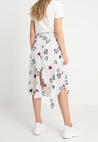 Gonna bianca asimmetrica con pois neri e motivi a cuore colorati, caratterizzata da uno spacco laterale e indossata con sneakers bianche.