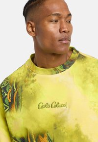 Gul sweatshirt med grønt og orange abstrakt mønster. Har ribbet krave, broderet logo og et blødt, struktureret stof.
