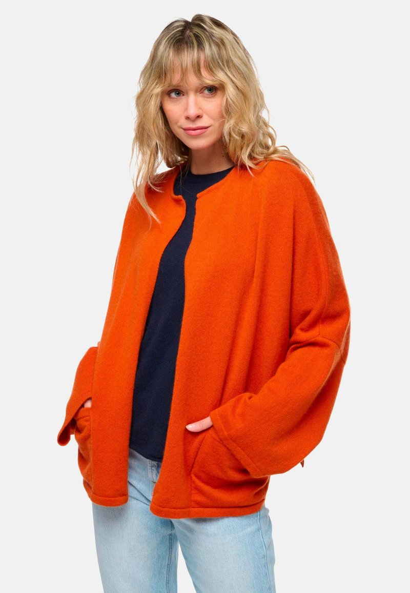 Cardigan en laine orange avec une coupe décontractée, ouvert sur le devant et doté de grandes poches. Texture douce, manches chauve-souris et col rond.
