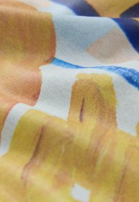 Gros plan sur un tissu avec un motif abstrait doux aux tons bleu, jaune et beige, montrant la texture et les plis.