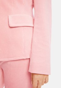 Rosa Cordblazer mit strukturiertem Finish, schmalem Revers und einer einzelnen aufgesetzten Tasche auf der linken Brustseite.