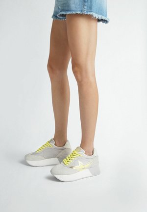 Sneaker grigi con suede testurizzato e pelle liscia, caratterizzati da lacci e dettagli gialli, e una suola bianca spessa con una leggera elevazione.
