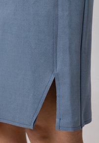 Jupe bleue en tissu texturé avec une fente sur un côté, finition propre et motif en relief diagonal.