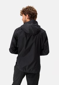 Giacca leggera nera con cappuccio, caratterizzata da una texture liscia e un'orlo posteriore leggermente più lungo, progettata per l'uso all'aperto.