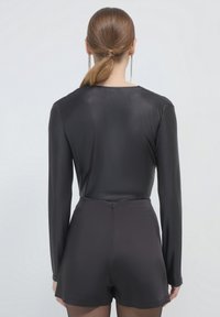 Body nero a maniche lunghe con una texture liscia, abbinato a pantaloni corti neri a vita alta con una cerniera posteriore discreta.