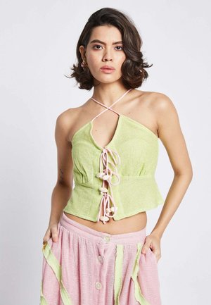 Top halter vert texturé avec un décolleté en V profond et une fermeture à nouer rose, agrémenté de perles décoratives. Associé à une jupe rose à boutons.