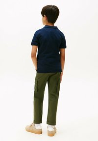 Marineblå polo t-shirt, grøn cargo bukser med sidelommer og beige sneakers. Korte ærmer, afslappet pasform og oprullede nederste kanter på bukserne.