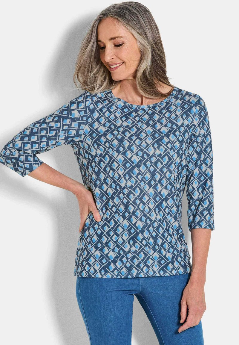 Top blu con motivo a stampa e maniche a tre quarti. Il design presenta forme geometriche in diverse tonalità di blu. Materiale morbido e leggero.