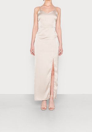 Kvinde i en cremefarvet satin natkjole med spaghetti stropper og en frontslids op til låret, iført matchende åbne tå-hæle.