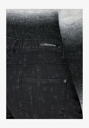 Schwarze Jeans aus Denim mit dezenten Buchstabenmustern, einem elastischen Bund und einem "#TrueSize"-Label auf der Rückseite. Verfügt über klassische Gesäßtaschen.