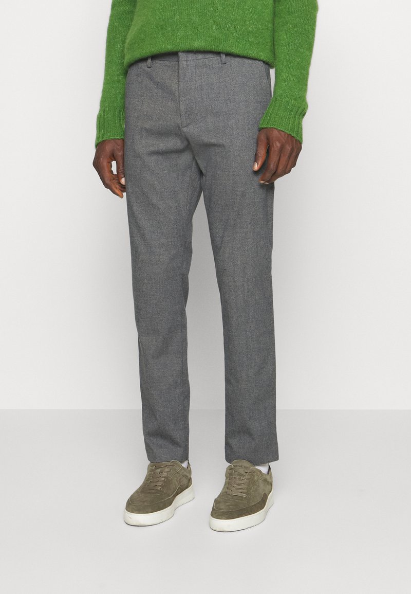 Grau melierte Wollmischungshosen mit taillierter Passform, kombiniert mit olivfarbenen Sneakers. Das Outfit wird mit einem grünen Strickpullover abgerundet.