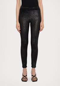 Čierne legíny s lesklým leopardím vzorom. Majú priliehavý strih a široký elastický pás. Nosia sa s čiernymi sandálmi na opätku.