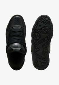 Scarpa da ginnastica nera con motivi decorativi sulla punta, lacci spessi e suola strutturata con forme circolari e triangolari.