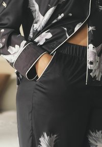 Set de pijama din satin negru, cu modele florale și de păsări albe, având o croială lejeră. Cămașa are o pipă albă contrastantă și un buzunar deschis.