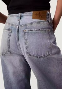Jeans in denim azzurro chiaro a vita alta, con una toppa marrone con il logo, due tasche posteriori e dettagli di cuciture a contrasto.