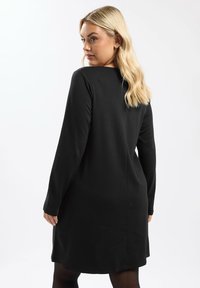 Schwarzes langärmeliges Kleid mit geradem Schnitt, das bis zur Mitte des Oberschenkels reicht. Mit Rundhalsausschnitt und glatter Textur. Minimalistisches Design ohne sichtbare Muster.