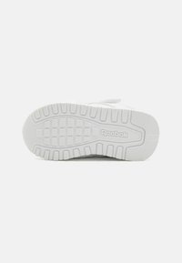 Hvit Reebok sneakersåle med et teksturert gummimønster, uttalte spor og preget logo. Rent og minimalistisk design.