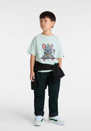 T-shirt verde chiaro con una grafica di un cane che indossa occhiali e una corona, pantaloni neri e scarpe bianche con dettagli verdi.
