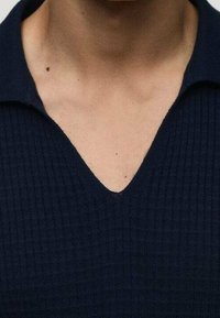 Tmavě modré polo s žebrovaným úpletem a výstřihem do V. Textura látky je hladká, s viditelným šitím podél límce a okrajů.