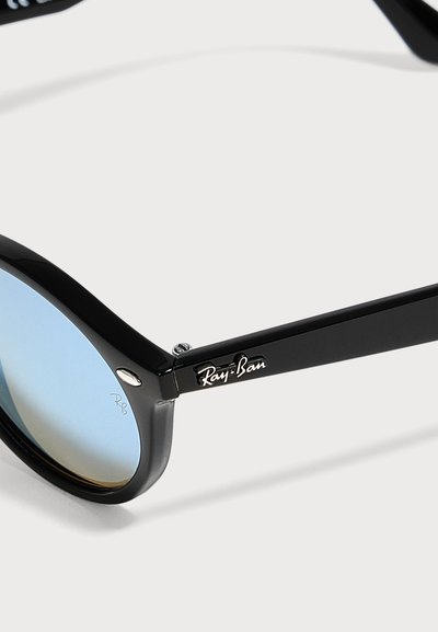 Крупен план на слънчеви очила Ray-Ban с черна рамка и сини градиентни лещи, видимо лого на марката на дръжката и в ъгъла на лещата.