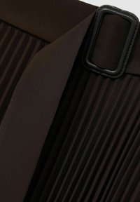 Tessuto plissettato nero con una cintura liscia dotata di una fibbia rettangolare nera. La texture è croccante con un aspetto strutturato.