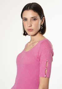 Top rosa adatto in un tessuto ribbed, con scollatura a barchetta e maniche corte arricchite da bottoni decorati.