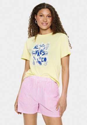 Chemise jaune à manches courtes avec des motifs marins bleus, accompagnée de shorts à rayures roses et blanches avec cordon de serrage. Texture en coton lisse.