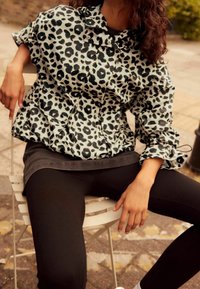 Luipaardprint, lichte pufferjack met een getailleerde pasvorm, elastische manchetten en een trekkoord bij de hals, gecombineerd met zwarte leggings.