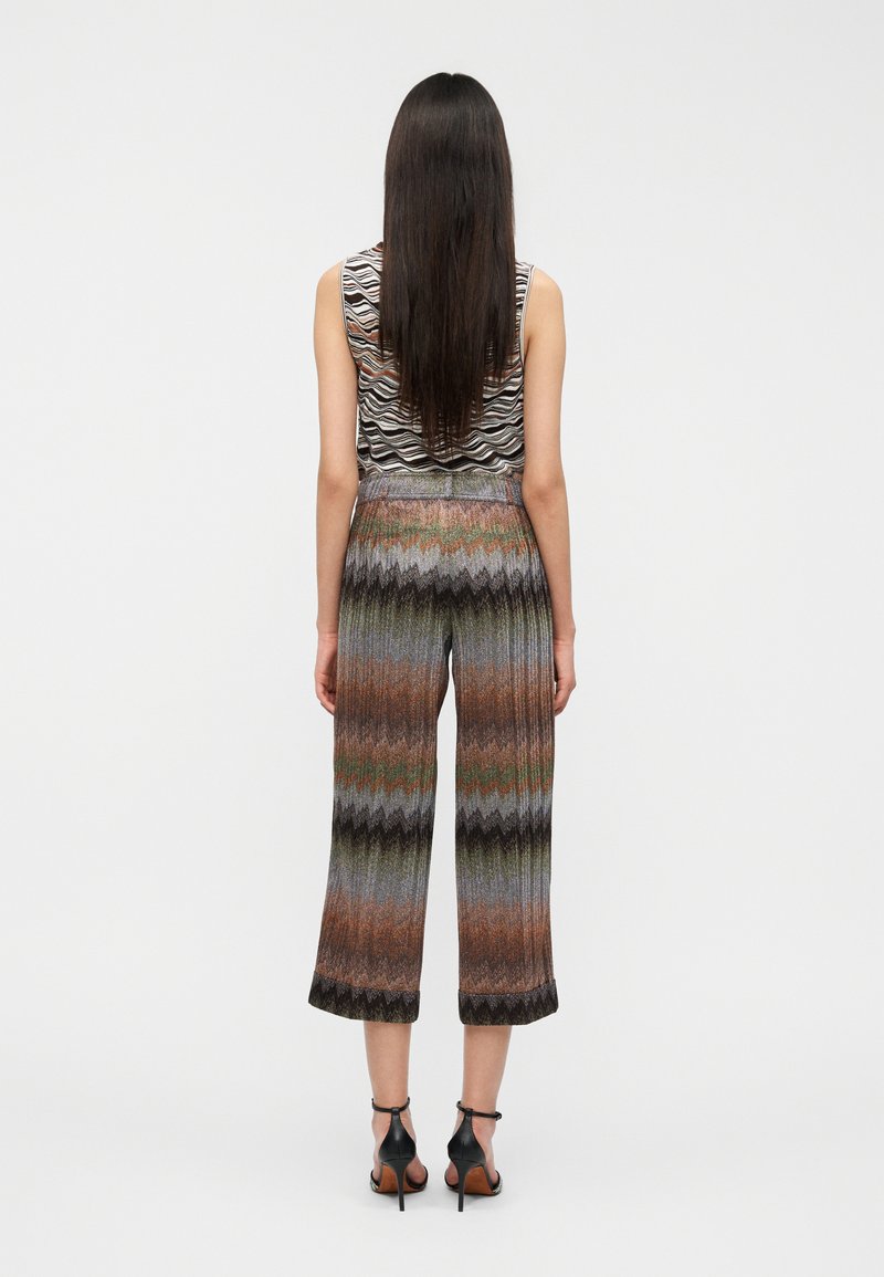 Knitted sleeveless top with a wavy black and white pattern; wide, colorful pants with a zigzag design and black accents at the hem.