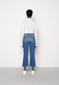 Höga blå denim jeans med vida ben, ljus blekning, bakfickor och en vit långärmad topp, kombinerat med vita sneakers.