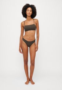 Zestaw bikini w ciemnooliwkowym kolorze z bandeau topem na cienkich ramiączkach oraz wysokim stanem majtek o minimalnym zakryciu. Gładka faktura materiału.