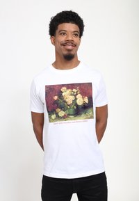 Hvid T-shirt med et farverigt print af et blomsterstilleben, med titlen "Skål med Pioner og Rosen," på en mørk baggrund.