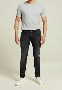 Grå t-shirt med korta ärmar, figursydd, i kombination med mörkblå jeans och vita sneakers. Slät tyg, subtila detaljer, klassisk silhuett.