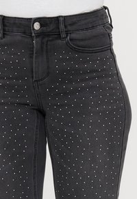 Svarta denimjeans med metalliska nitar arrangerade i ett prickmönster över framsidan. Klassisk design med fem fickor och dragkedja.