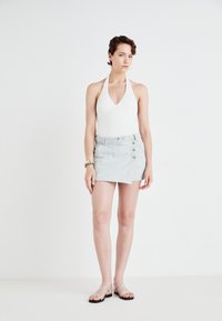 Bijeli halter bodysuit, mini suknja od denima s plavim prugama, bočnim gumbima i dizajnom omotnice. Srebrne sandale s remenčićima upotpunjuju outfit.