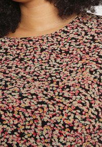 Tela negra con un estampado floral que presenta pequeñas flores en tonos rosa, amarillo y verde. Cuello redondo y textura suave.
