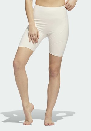 High-waisted beige fietsbroeken van rekbaar materiaal met een gladde textuur, voorzien van schuine naden en een klein merkembleem.