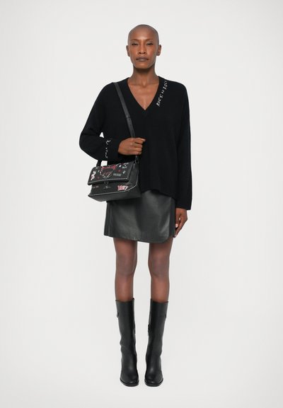 Sort oversized sweater med "Rock 'n' Roll" detalje, tætsiddende sort læder mini skirt, og knæhøje sorte læder støvler. Sort dekorativ håndtaske.