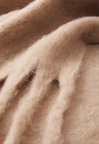 Tesătură din lână bej cu o textură moale și pufoasă, având pliuri și ondulații delicate care creează un aspect curgător și stratificat.