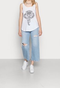 Top blanco de tirantes con gráfico de elefante, combinado con jeans anchos de cintura clara y rotos, y zapatillas blancas. Presenta un corte relajado y un estilo casual.
