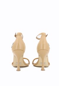 Sandali beige con tacco alto e cinturino alla caviglia, finitura in pelle liscia, punta affusolata e tacco a stiletto. Presentano borchie decorative sui lati.